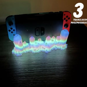 Peut inclure: Un support en cristal arc-en-ciel pour une console Nintendo Switch. Le support est en plastique translucide phosphorescent et brille dans le noir. Le support est étiqueté "Translucide Phosphorescent" et "3".