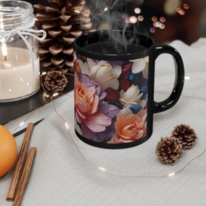 May include: Black coffee mug with a floral design featuring pink, white, and purple flowers. The mug is filled with coffee and steam is rising from the top.