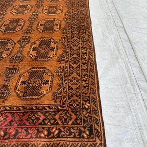 May include: A rectangular runner rug featuring a warm orange background with repeating dark brown octagonal geometric motifs. The border displays intricate black and orange patterns, and the short end is finished with grey fringe tassels.