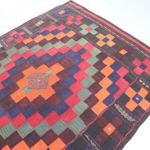 May include: A colorful rug with a geometric pattern in shades of red, orange, green, blue, and black. The rug has a traditional design with intricate details.