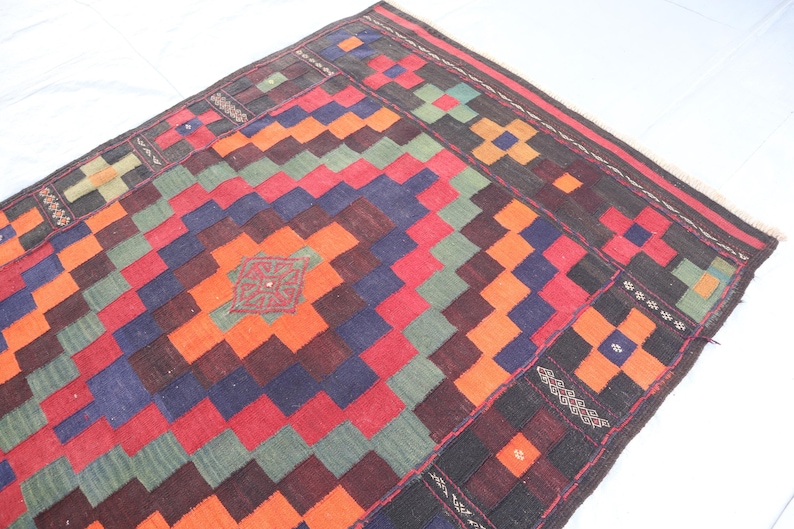 May include: A colorful rug with a geometric pattern in shades of red, orange, green, blue, and black. The rug has a traditional design with intricate details.