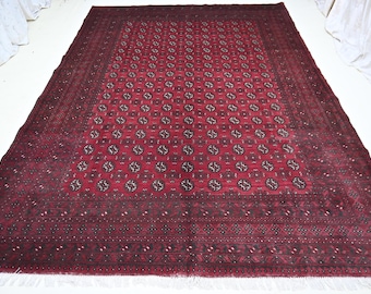 Könnte beinhalten: Ein rechteckiger Teppich mit einer tiefroten Grundfarbe und einem sich wiederholenden Muster aus dunklen, kreisförmigen geometrischen Motiven. Der Teppich ist von einer breiten, komplexen Bordüre in Schwarz und Dunkelrot umrahmt und hat weiße Fransen.