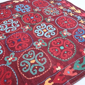 May include: A red, blue, green, and yellow patterned rug with a repeating circular design. The rug is made of wool and has a hand-woven texture.