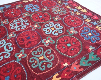 May include: A red, blue, green, and yellow patterned rug with a repeating circular design. The rug is made of wool and has a hand-woven texture.