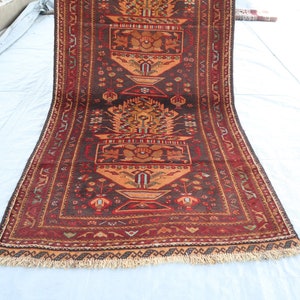 May include: A traditional Persian rug with a dark brown background and intricate floral patterns in shades of red, orange, and yellow. The rug has a fringed edge and is made of wool.
