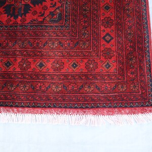 May include: A red rug with a black and white geometric pattern. The rug has a white fringe around the edges.
