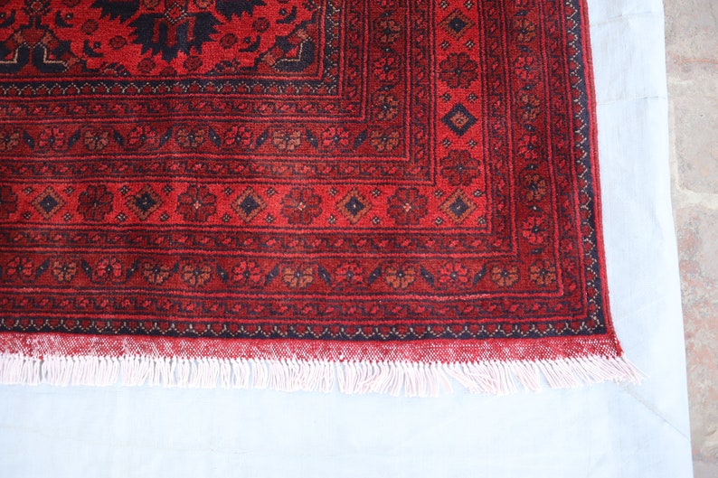 May include: A red rug with a black and white geometric pattern. The rug has a white fringe around the edges.
