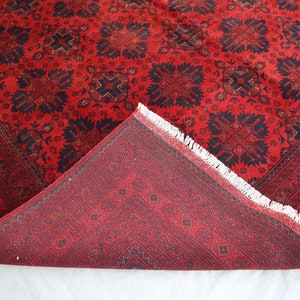 May include: A red and black patterned rug with a fringe border. The rug is folded in half, showing the back side, which has a smaller, more intricate pattern.