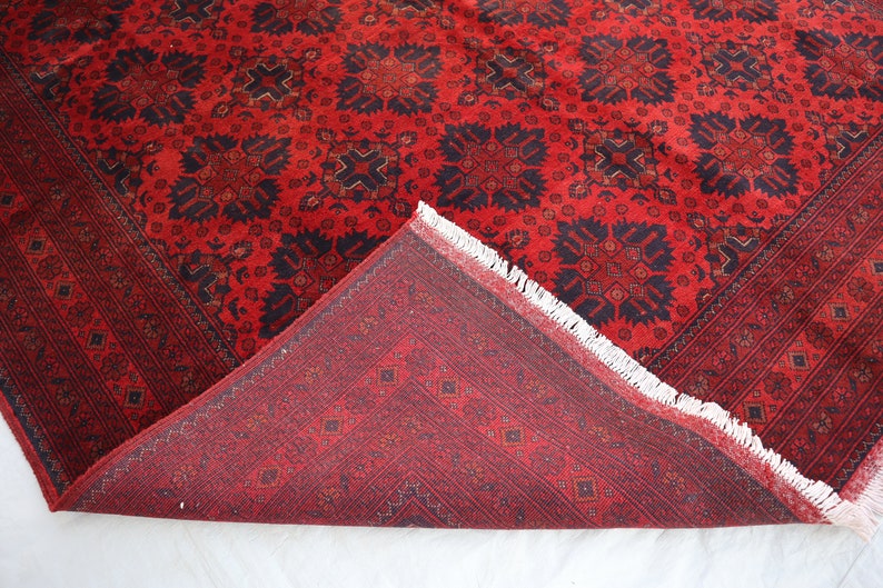 May include: A red and black patterned rug with a fringe border. The rug is folded in half, showing the back side, which has a smaller, more intricate pattern.