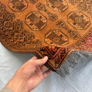 May include: A rectangular rug featuring a warm orange background with repeating dark brown octagonal geometric patterns and intricate border designs. The rug has a thick pile texture and includes a short, light gray fringe along the edge.