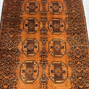 May include: A rectangular area rug featuring a vibrant orange background with a repeating pattern of dark brown octagonal medallions. The rug includes intricate geometric borders and stylized motifs throughout the central field design.