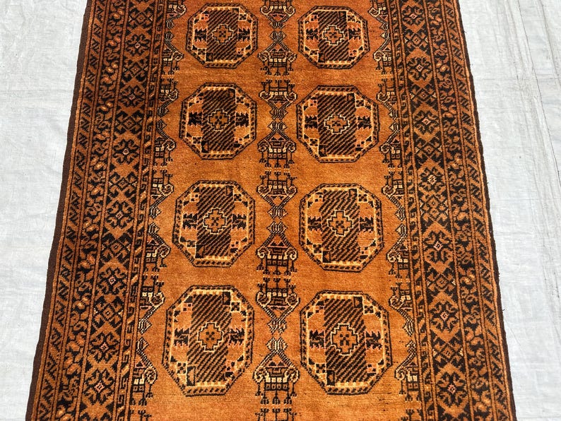 May include: A rectangular area rug featuring a vibrant orange background with a repeating pattern of dark brown octagonal medallions. The rug includes intricate geometric borders and stylized motifs throughout the central field design.
