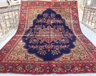 Könnte beinhalten: Ein traditioneller persischer Teppich mit einem dunkelblauen Zentrum und aufwendigen Blumenmustern. Der Teppich hat einen roten Rand mit einem Blumendesign und einen cremefarbenen Innenrand.