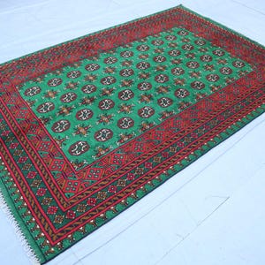 K&ouml;nnte beinhalten: Ein gr&uuml;ner und roter Teppich mit geometrischem Muster. Der Teppich hat einen Fransenrand.