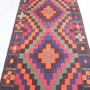 May include: A colorful rug with a geometric pattern in shades of red, orange, green, blue, and brown. The rug has a border with a repeating design.