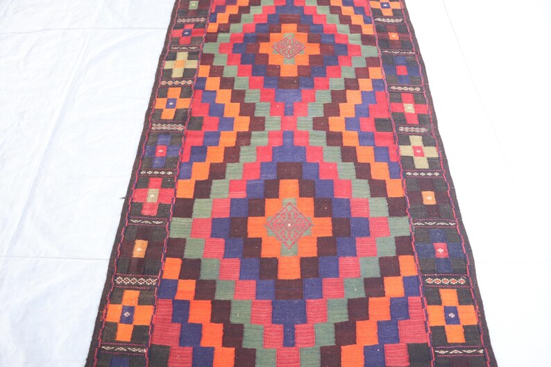 May include: A colorful rug with a geometric pattern in shades of red, orange, green, blue, and brown. The rug has a border with a repeating design.