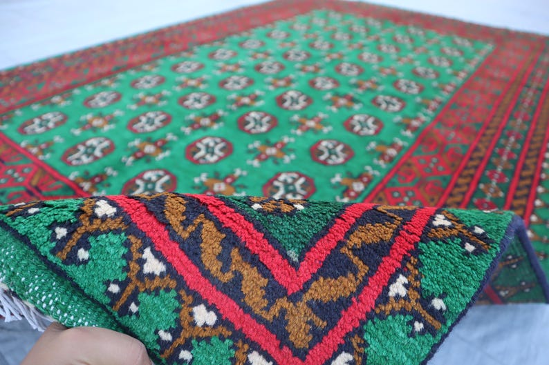 K&ouml;nnte beinhalten: Ein gr&uuml;ner und roter Teppich mit geometrischem Muster. Der Teppich hat einen Fransenrand und ist aus Wolle.