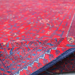 May include: A red and blue rug with a traditional Persian design. The rug is folded in half, showing the intricate details of the pattern.