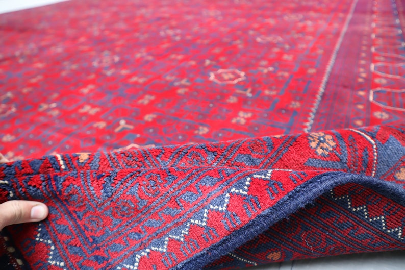 May include: A red and blue rug with a traditional Persian design. The rug is folded in half, showing the intricate details of the pattern.