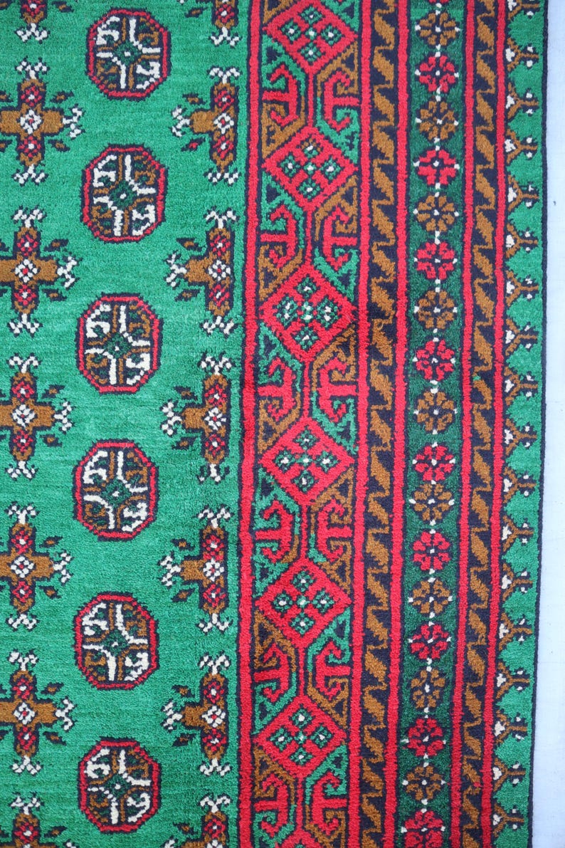 K&ouml;nnte beinhalten: Ein gr&uuml;ner Teppich mit einem roten, braunen und gr&uuml;nen Rand. Der Teppich hat ein sich wiederholendes Muster aus geometrischen Formen.