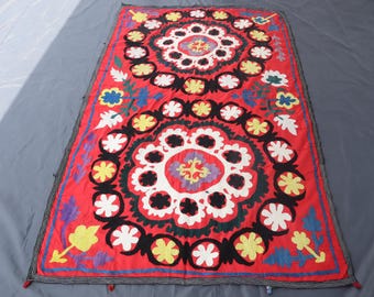 May include: A rectangular textile wall hanging featuring a vibrant red background with two large, circular floral motifs. The design includes black, white, yellow, blue, and purple embroidered patterns of stylized flowers and leaves throughout.