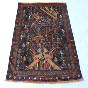 May include: A rectangular area rug featuring a dark blue background with a central tree motif and stylized bird figures. The design includes intricate geometric patterns in red, tan, and cream, finished with a short fringe along the top and bottom edges.
