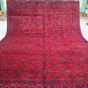 May include: A red rug with a detailed floral pattern and a blue border. The rug is folded in half and laid out on a white surface.