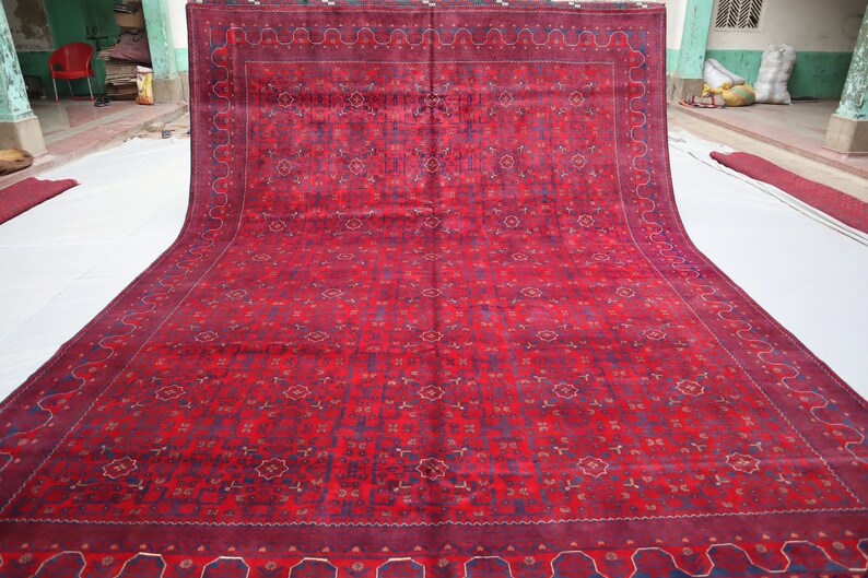 May include: A red rug with a detailed floral pattern and a blue border. The rug is folded in half and laid out on a white surface.