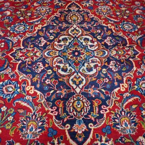 Puede incluir: Una alfombra rectangular con un fondo rojo intenso y un gran medall&oacute;n central intrincado en azul marino. El dise&ntilde;o incluye elaborados motivos florales y de enredaderas en tonos azul claro, crema, amarillo y verde por toda la superficie.