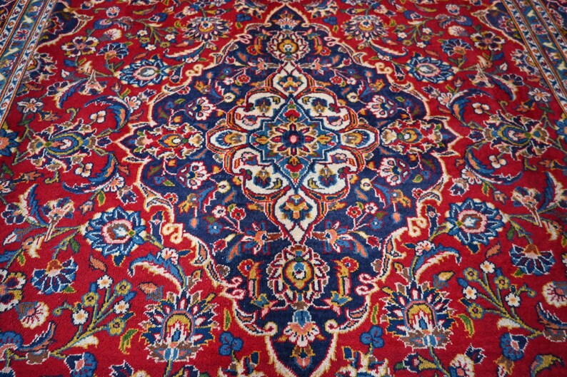Puede incluir: Una alfombra rectangular con un fondo rojo intenso y un gran medall&oacute;n central intrincado en azul marino. El dise&ntilde;o incluye elaborados motivos florales y de enredaderas en tonos azul claro, crema, amarillo y verde por toda la superficie.