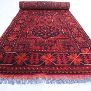 May include: A red and black rug with a traditional Persian design. The rug has a fringed border and is rolled up.