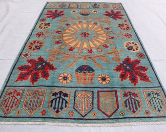 May include: A teal blue rug with a central medallion featuring a sunburst design. The rug has a border with repeating floral motifs and stylized leaves in shades of red, yellow, and blue.