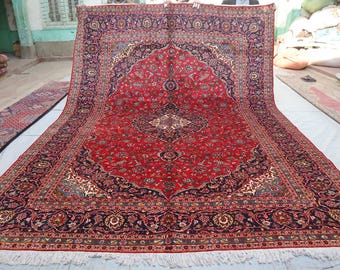 May include: A large rectangular area rug featuring a vibrant red central field with an intricate navy blue medallion and floral patterns. The wide border is navy blue with detailed floral motifs in red, cream, and gold, finished with white fringe.