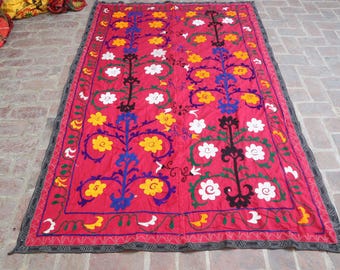 May include: A vibrant red textile with a detailed floral pattern. The design features yellow, white, and blue flowers, with black and green accents. The border is a dark gray with a geometric pattern.
