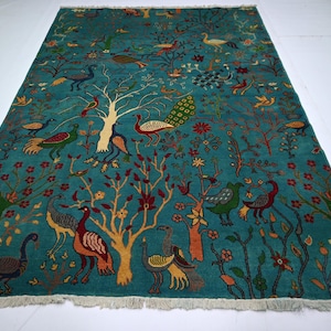 May include: Teal-colored area rug with a detailed pattern of trees, birds, and floral elements. The rug features various birds, including peacocks, and a fringe along the bottom edge. The design is intricate and colorful.