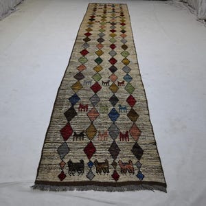 May include: A long, rectangular rug with a diamond pattern in various colors, including red, blue, green, and yellow. The rug features small animal figures within the diamond shapes and has a fringed edge.