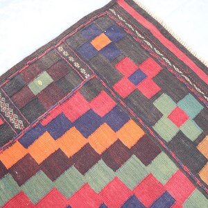 May include: A colorful rug with a geometric pattern in shades of red, orange, green, blue, and black. The rug has a fringe border.