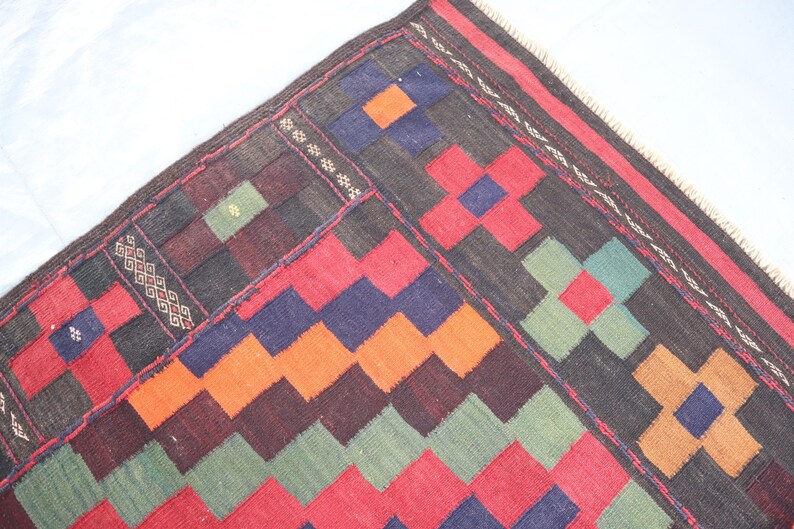 May include: A colorful rug with a geometric pattern in shades of red, orange, green, blue, and black. The rug has a fringe border.