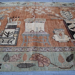 Puede incluir: Una alfombra rectangular grande con un diseño detallado. La alfombra presenta un campo central de tonos marrones cálidos con motivos florales y geométricos estilizados. El borde es verde suave con patrones de hojas y flores. El diseño de la alfombra incluye jarrones y mesas.