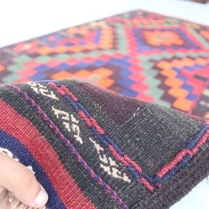 May include: Close-up of a dark brown, red, and blue patterned rug with fringe. The rug has a geometric design with a black background.