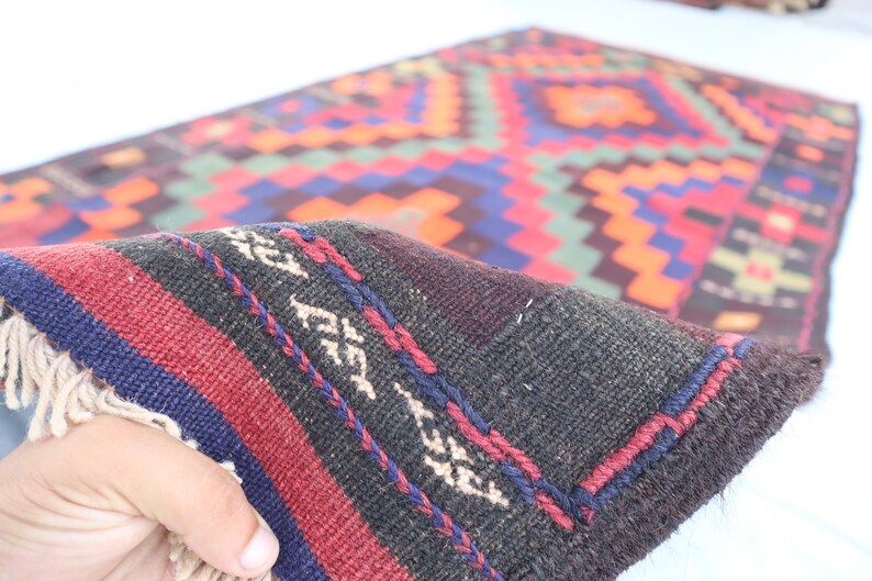May include: Close-up of a dark brown, red, and blue patterned rug with fringe. The rug has a geometric design with a black background.