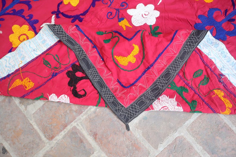 K&ouml;nnte beinhalten: Ein leuchtend rotes Textil mit aufwendigen Stickereien in Wei&szlig;, Gelb, Blau und Schwarz. Das Design zeigt florale und geometrische Muster mit einem detaillierten Rand. Der Stoff ist gefaltet und zeigt die detaillierte Handwerkskunst.