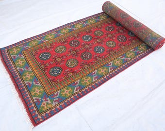Puede incluir: Una alfombra roja, verde, azul y amarilla con un diseño geométrico. La alfombra está enrollada y tiene flecos en los bordes.