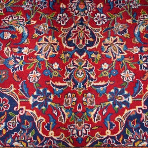 Puede incluir: Una alfombra tejida con un patr&oacute;n floral denso y complejo sobre un fondo rojo vibrante. El dise&ntilde;o incluye arreglos sim&eacute;tricos de flores estilizadas y enredaderas en tonos azul oscuro, azul claro, blanco y toques de color dorado.