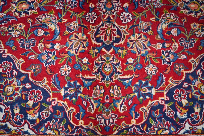 Puede incluir: Una alfombra tejida con un patr&oacute;n floral denso y complejo sobre un fondo rojo vibrante. El dise&ntilde;o incluye arreglos sim&eacute;tricos de flores estilizadas y enredaderas en tonos azul oscuro, azul claro, blanco y toques de color dorado.