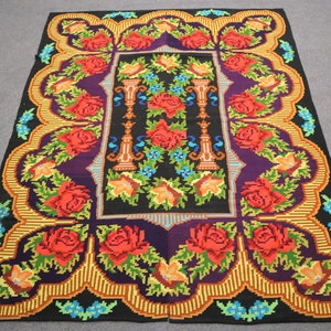 May include: A colorful rug with a floral design. The rug features red roses, green leaves, and yellow flowers on a black background. The rug has a border of gold and orange stripes.