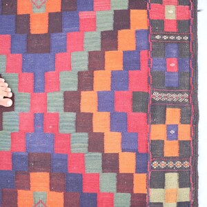 May include: A colorful woven rug with a geometric pattern in shades of red, orange, green, blue, and black. The rug has a border with intricate designs.