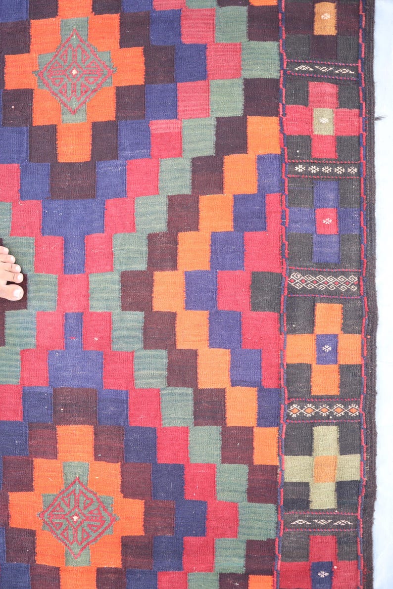 May include: A colorful woven rug with a geometric pattern in shades of red, orange, green, blue, and black. The rug has a border with intricate designs.