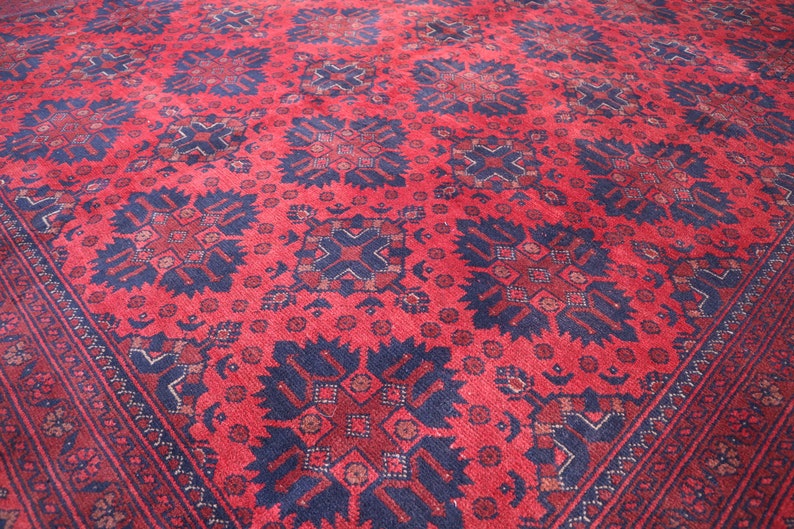 May include: A red rug with a blue and white geometric pattern. The rug has a traditional design with intricate details.