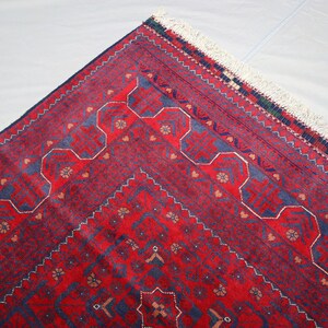 May include: A red and blue patterned rug with a white fringe. The rug has a geometric design with intricate details.